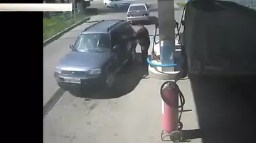 Мужчина, наливая бензин в крышу грузовика на заправке, закурил