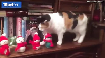 Кошка скидывает с камина праздничные фигурки